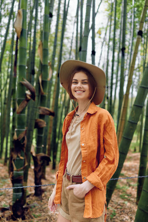 Woman smile bamboo hat orange forest portrait of a young traveler in casual clothing, straw hat and orange shirt among tall bamboo stalks, nature walk and relaxed outdoor lifestyle.の写真素材