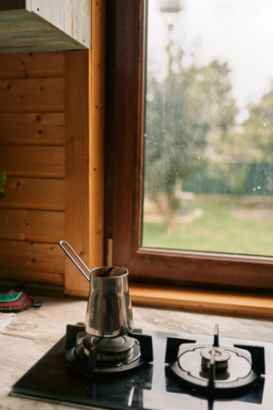 Calm kitchen scene shows a gas stove with a metal pot on the burner, framed by warm wood panels and a bright window, capturing a cozy home atmosphere.の写真素材