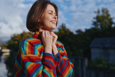 Woman smiling in a colorful rainbow sweater and short hair outdoors, young adult enjoying autumn...