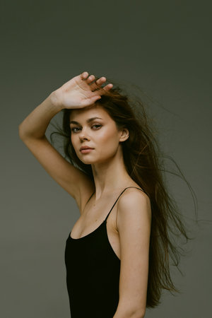 Portrait of a young woman with long hair shielding her eyes, wearing a black tank top against a...