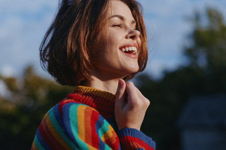 woman smiling in her mid twenties with short brown hair, wearing a colorful striped sweater outdoors in warm sunlight, joyful expression, casual outfit, lifestyle portrait for travel and fashionの写真素材