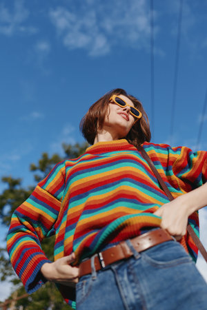 Woman in a colorful striped sweater and yellow sunglasses under blue sky, young adult with short...