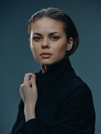 Portrait of a young woman with slicked-back hair wearing black clothing, showing a calm and...