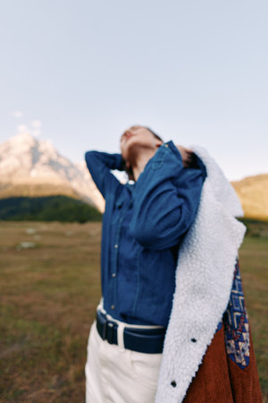woman mountain nature jacket denim travel outdoors portrait of young model in field, casual style with coat over shoulder, looking up to sky in scenic landscape for adventure and relaxationの写真素材