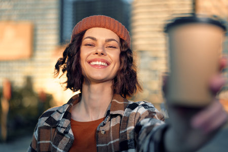 Woman smile coffee urban candid authenticity golden lifestyle portrait of a young woman holding a takeaway cup during golden hour glow, joyful mindful living and emotional storytelling in city.の写真素材