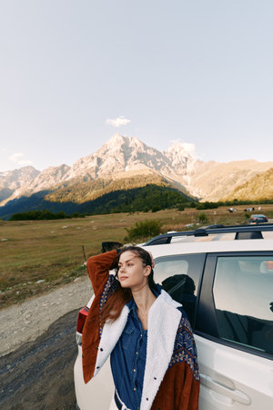 Woman by car parked in alpine mountain landscape during travel roadtrip, portrait of relaxed...