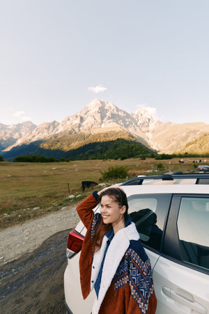 Woman car mountains travel portrait roadtrip landscape nature young woman leaning on white SUV smiling with jacket, scenic countryside road and panoramic mountain view under open sky.の写真素材