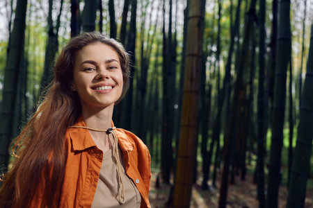 Woman smile forest bamboo portrait outdoors nature longhair, young woman smiling in a bamboo grove wearing an orange jacket, natural light and relaxed expression for outdoor lifestyle scene.の写真素材