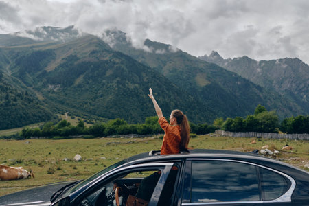 Woman in orange top leans out of a car window in a vast countryside with distant mountains, smiling...
