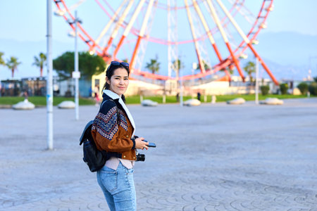Woman with backpack walking near a ferris wheel, outdoors daytime scene, casual style, urban leisure...