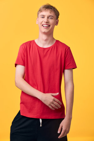 Smiling man in a red t shirt stands against a bright yellow background, radiating casual confidence and friendly energy for lifestyle, fashion or advertising imageryの写真素材