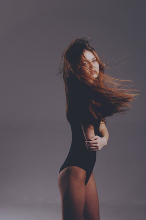 Woman in black bodysuit with flowing hair standing against gray background, expressive and mysterious moodの写真素材