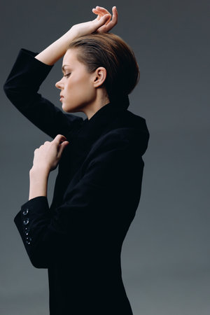 stylish woman in black blazer posing sideways with closed eyes and serene expression against gray backgroundの写真素材