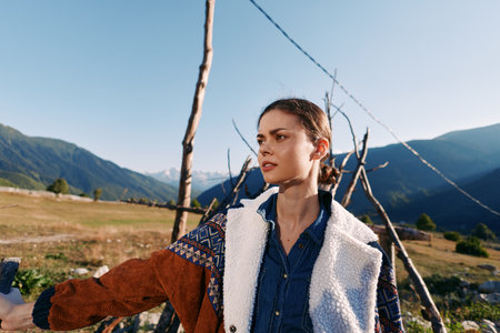 Woman portrait in mountains outdoors and nature, wearing warm textured jacket in rural countryside. Young traveler gazes into distance with sunlight, hiking lifestyle and serene landscape.の写真素材