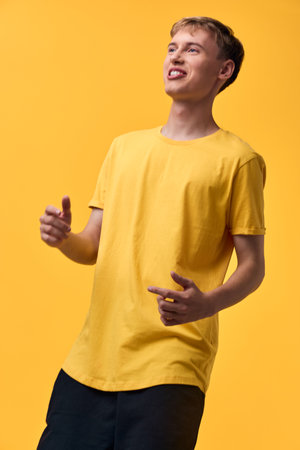 Cheerful man in a yellow shirt on a vibrant yellow backdrop, giving a thumbs up with a confident pose, conveying positivity, casual fashion, and everyday lifestyle for marketing and stock useの写真素材