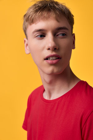 Young man wearing a red shirt against a warm yellow background, showcasing casual style, thoughtful expression and clean studio lighting. Modern lifestyle vibe with strong color contrast and minimalの写真素材