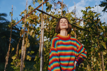 Young adult woman smiling in a rainbow striped sweater in a tropical garden portrait, casual outfit, short hair, joyful mood, sunlight, lifestyle and fashion outdoor sceneの写真素材
