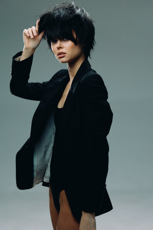 Young woman with short black hair wearing a black blazer posing confidently on a neutral backgroundの写真素材