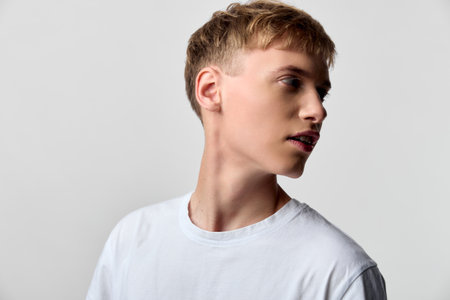 Young man in a white tee turns his head to the side, presenting a calm studio vibe with a clean...