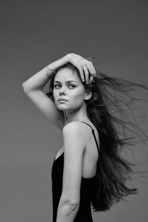 Black and white portrait of a young woman with long flowing hair and a contemplative expression against a plain background.の写真素材