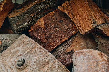 Firewood stacked logs woodpile wooden texture rustic split logs bark fuelwood closeup of dried fireplace wood, earthy brown tones and rough wood grain for cabin heating, winter supply and decor.の写真素材
