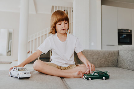 A focused boy sitting on a sofa, playing with toy cars in a bright living room filled with natural light. His playful imagination brings joy and creativity to life.の写真素材