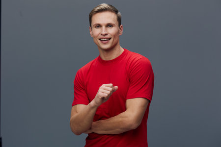 Cheerful young man wearing red t-shirt smiling and pointing at himself on plain gray background. Happy, confident, casual, casualwear, positive vibe, studio portrait, people lifestyle concept.の写真素材