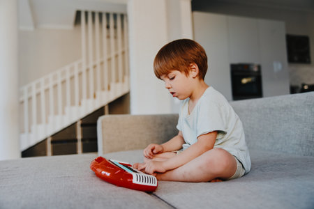 A focused boy engaging with a colorful toy, sitting on a cozy couch in a modern living room, showcasing creativity and playful imagination.の写真素材