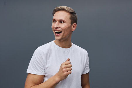 smiling young man wearing white t-shirt looking aside standing on gray background digital nomad lifestyle remote work conceptの写真素材