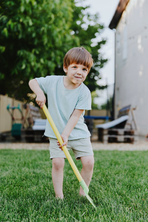 Playful boy enjoying outdoor activities, wearing a light blue shirt and shorts, smiling while using...