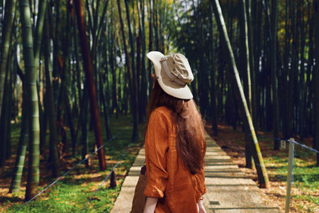 woman hat forest bamboo path back walking nature travel rear view of a female traveler wearing a sun...