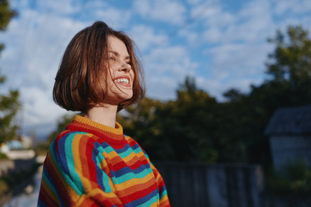 Woman smiling young adult in striped sweater outdoor portrait, a cheerful 20s brunette with bob haircut leaning into sunlight, casual outfit for colorful travel lifestyle and cozy fashion mood.の写真素材