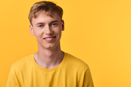 Young man in a yellow t shirt stands against a vibrant yellow background, smiling in a casual studio shot that highlights cheerful mood, bright color and approachable styleの写真素材