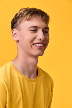 Happy, smiling male in a yellow tee against a bright yellow studio backdrop, close-up shot highlighting cheerful mood and bold color for lifestyle and fashion useの写真素材