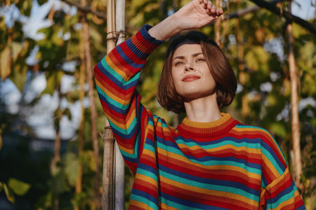 Woman in striped sweater with bob haircut smiling and leaning against bamboo in tropical outdoor setting, casual outfit, warm sunlight, lifestyle travel and fashion portrait.の写真素材