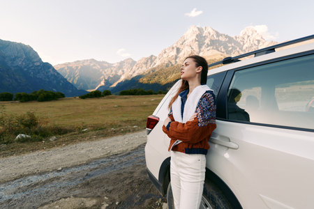 woman car mountains road travel nature landscape portrait. Young woman leans on white SUV at roadside, enjoying a scenic mountain view during a road trip, outdoor adventure and freedom.の写真素材