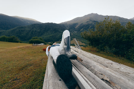 Person on bench in mountains nature relax boots meadow outdoor lying on wooden plank with jacket, peaceful landscape, distant peaks and green valley for weekend escape and rest.の写真素材