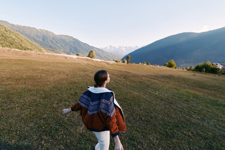 Woman walking in a meadow toward mountains across open landscape, nature hiking outdoors travel...