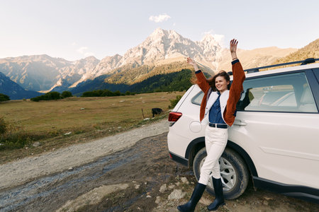 Woman by car in mountains, travel and nature road in countryside with raised arms, smiling and...