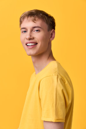 Smiling man in a bright yellow shirt stands against a bold yellow backdrop, conveying positivity,...