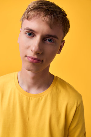 Closeup of a young man in a yellow shirt against a bright yellow background, showcasing a calm smile and casual style, perfect for lifestyle, fashion, and positive mood imagery in advertising,の写真素材