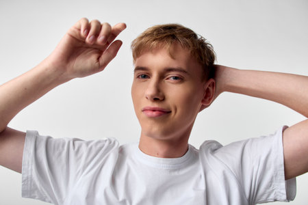 Casual young man in a white t shirt, arms raised behind his head, relaxed smile, studio lighting, clean background, everyday lifestyle mood and confident posture.の写真素材