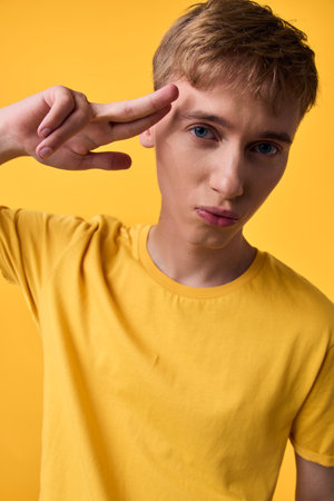 Young man in a yellow t shirt making a peace sign against a matching yellow backdrop, confident casual vibe suitable for lifestyle, fashion, and self expression themesの写真素材