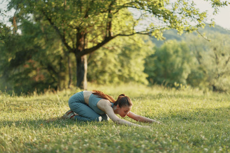 Woman practicing yoga in nature, wearing sportswear, expressing calmness among greenery under sunlight, highlighting wellness and fitness conceptsの写真素材