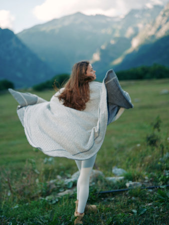 Woman wrapped in blanket spinning in mountain meadow, portrait capturing movement and freedom in nature and outdoors. Long hair, grass underfoot, cozy layers and soft light.の写真素材