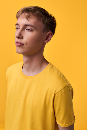 Yellow shirted male model with calm expression stands against a matching yellow backdrop, soft lighting highlights color harmony and minimalist studio compositionの写真素材