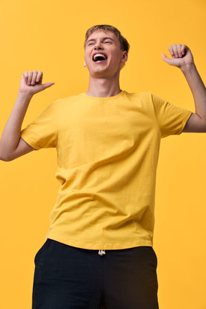 Celebration, excitement, energy as a yellow shirted man raises fists in triumph against a bold orange backdrop, joyful expression fills the frame with optimismの写真素材