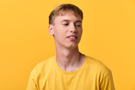 Man in yellow t shirt smiling slightly in a studio with a solid yellow backdrop, casual lifestyle image conveying warmth, brightness, and contemporary fashion vibesの写真素材