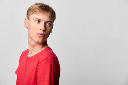 Young man in red shirt looks to the side with a thoughtful gaze in a clean studio, conveying curiosity, mood, and calm confidence for lifestyle projectsの写真素材