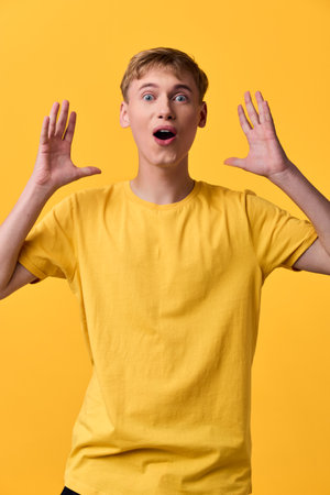 Surprised astonishment excited yellow shirt studio lighting arms raised expression youth casual pose energy and wonder captured in a bright, vibrant, upbeat moment with a male model in a candidの写真素材